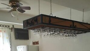Une cuisine avec un réfrigérateur blanc, un pare-feu en carrelage, un coin bar avec des tabourets en osier et un ventilateur de plafond.