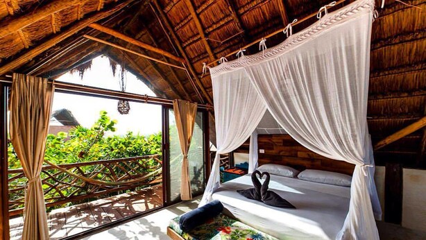Ein Zimmer mit einem Himmelsbett, einem Balkon mit Blick und einer Holzbalkendecke.