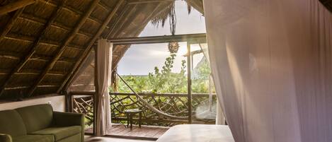 A room with a bed, a green sofa, and a view of greenery outside.