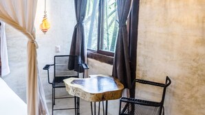 Ein Zimmer mit einem Bett, einem kleinen runden Tisch mit zwei Stühlen, einer Hängelampe und einem Fenster mit Vorhängen.