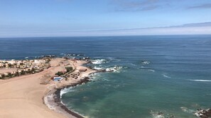 An aerial view of a coastal area with a beach, rocky shoreline, and buildings.