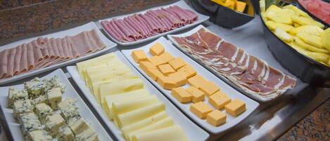 A buffet with various cheeses, meats, and fruits.