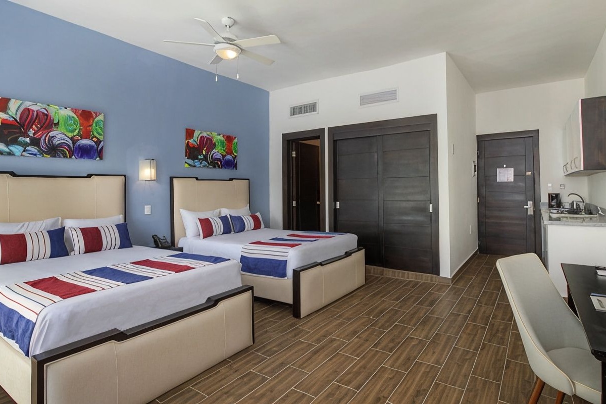 A hotel room with two beds, a desk, a chair, and a ceiling fan.