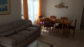 Un salon comprenant un canapé, une table basse avec un plateau en verre et un coin repas avec une table et des chaises en bois.