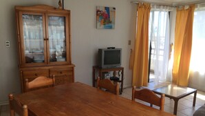 Un coin repas avec une table et des chaises en bois, un meuble avec des portes en verre, un téléviseur posé sur un meuble et un tableau accroché au mur.