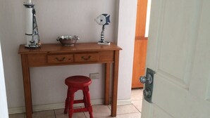 Une petite pièce avec un bureau en bois, un tabouret rouge, un tableau encadré et un sol carrelé.