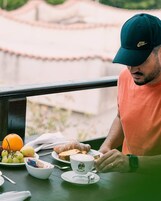 Una persona seduta a un tavolo con un pasto, una tazza e un orologio.