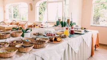 A buffet table with various food items and baskets, set in a room with large windows and a white tablecloth.