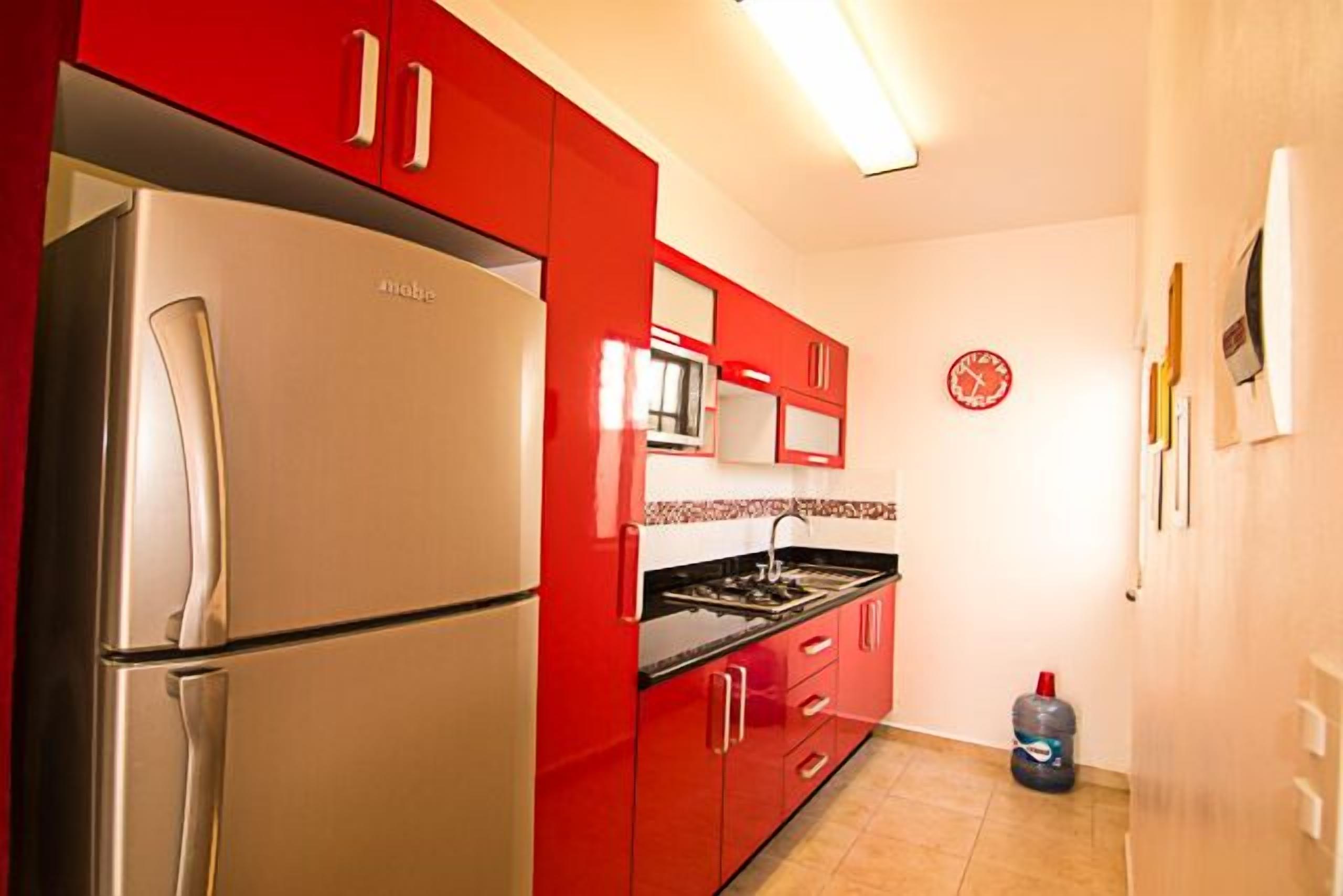 Une cuisine avec des meubles de rangement rouges, un réfrigérateur en acier inoxydable, un four à micro-ondes et une cuisinière à gaz.
