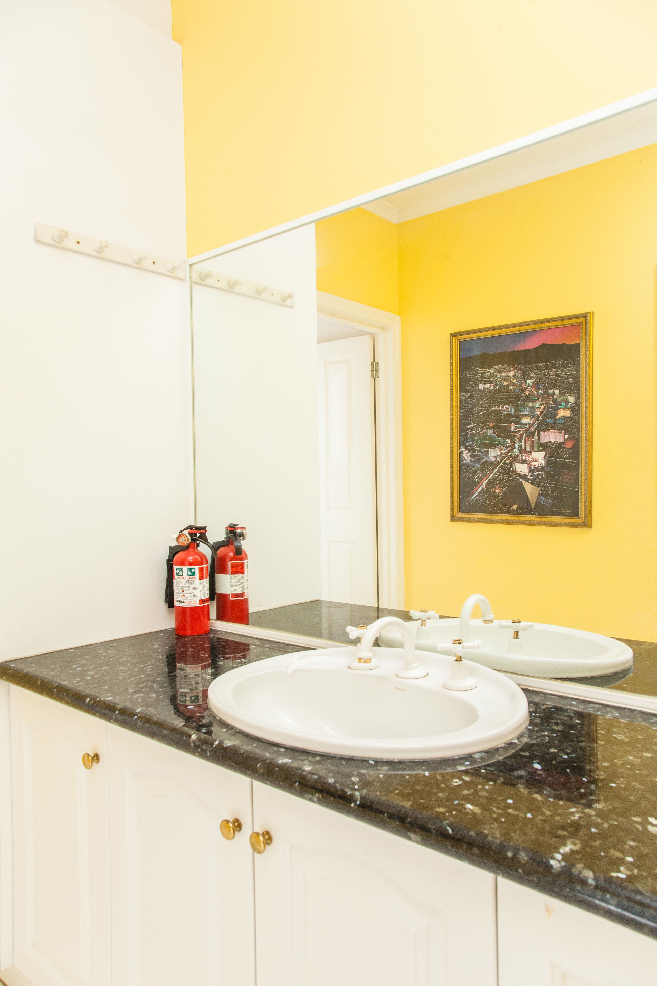 A bathroom with two sinks, a large mirror, and two fire extinguishers on the counter.