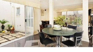 A spacious living area with a round table and chairs, a sofa, and a large window with curtains. - Abbotsford Private Rooms & Pods @ 15 Charles Homestay (Abbotsford)