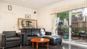A living room with a black leather sofa, a wooden coffee table, and a large window with curtains. - Abbotsford Private Rooms & Pods @ 15 Charles Homestay (Abbotsford)