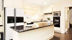 A modern kitchen with white cabinetry, a granite countertop, and built-in appliances including a refrigerator, microwave, and oven. - Abbotsford Private Rooms & Pods @ 15 Charles Homestay (Abbotsford)