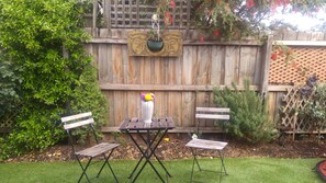 A wooden fence with a decorative metal plaque, a small table with two chairs, and a potted plant with flowers.