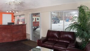 A reception area with a red wall, a reception desk, a leather sofa, and a large window with a view of a snowy street. - Budget Inn (Caldwell)