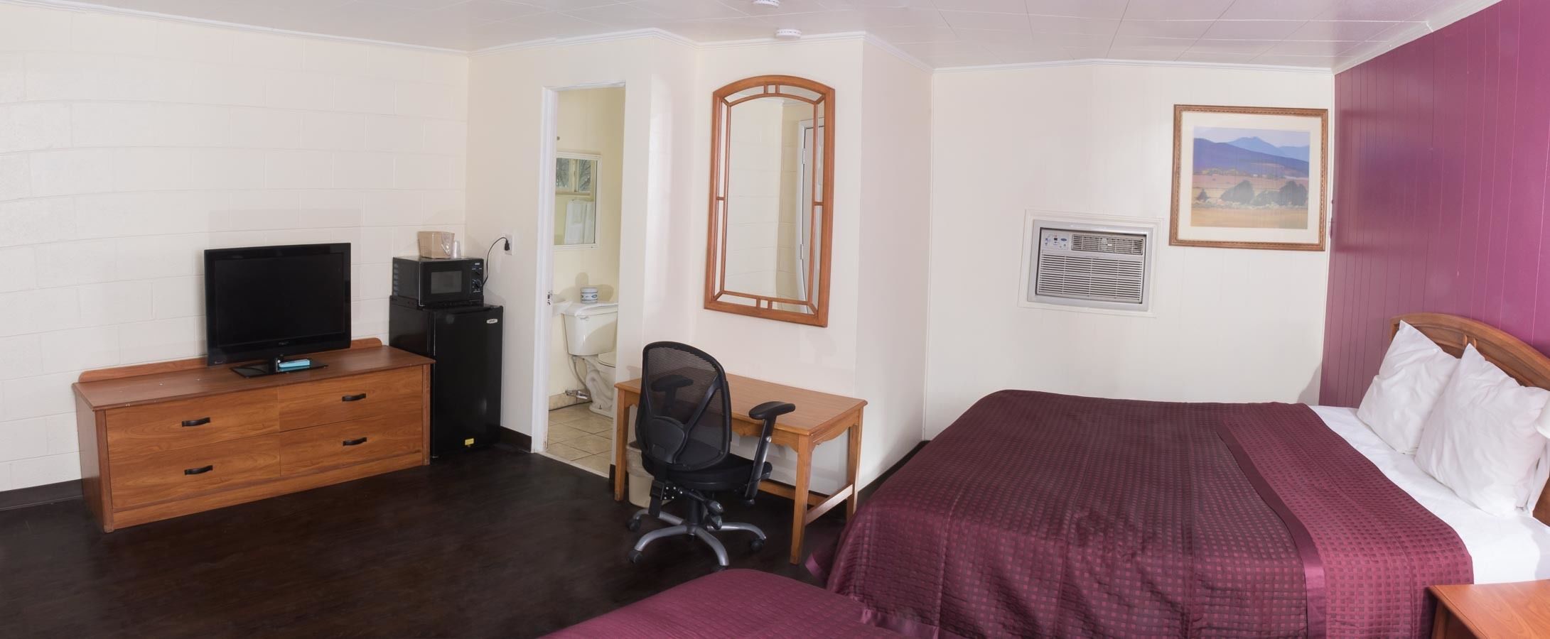 Una habitación de hotel con cama, escritorio, silla, televisión y espejo.