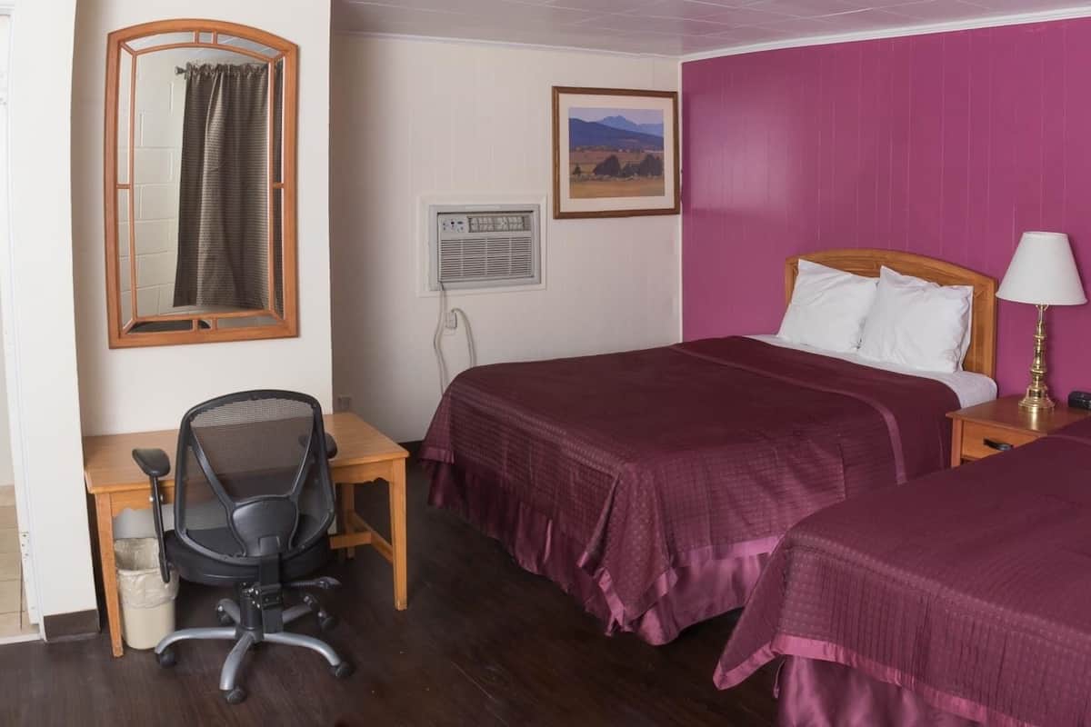 Une chambre avec deux lits, un bureau, une chaise, une fenêtre avec des rideaux, un tableau au mur et un appareil de climatisation.