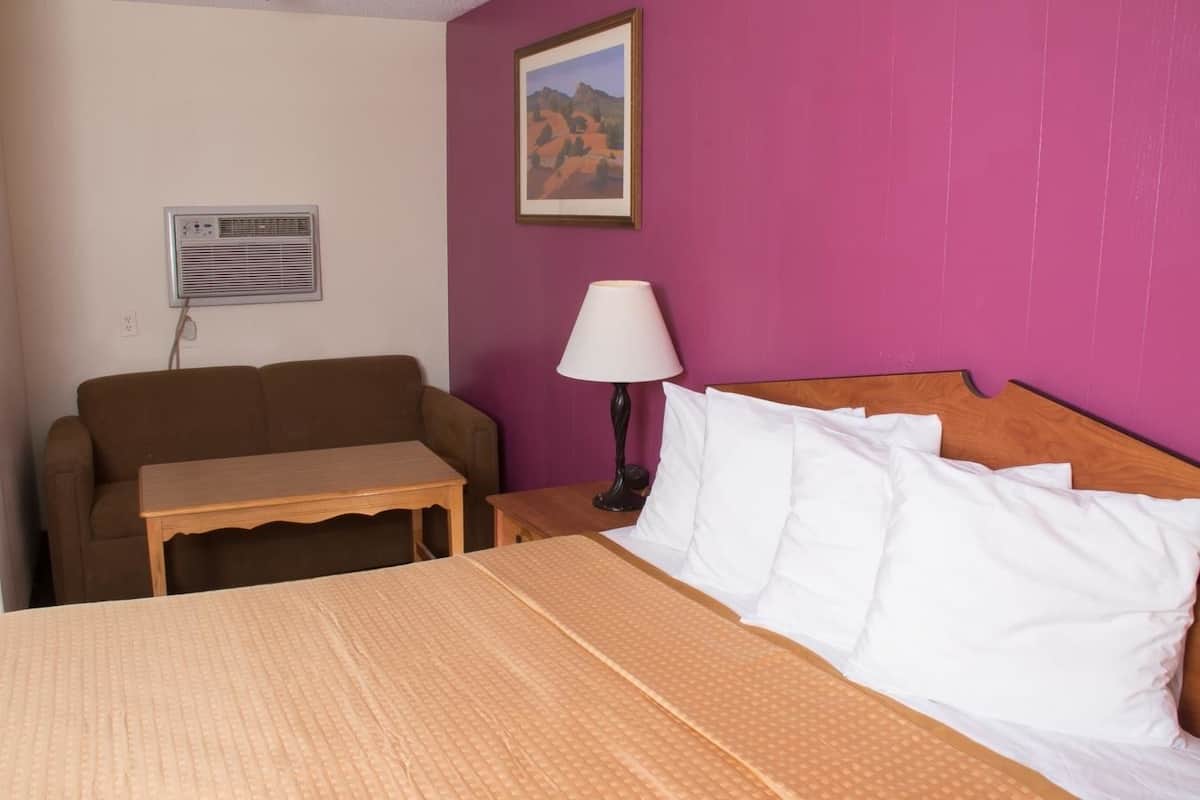 Une chambre d’hôtel comprenant un lit, une table de chevet en bois, une table, une lampe, un canapé et un appareil de climatisation.