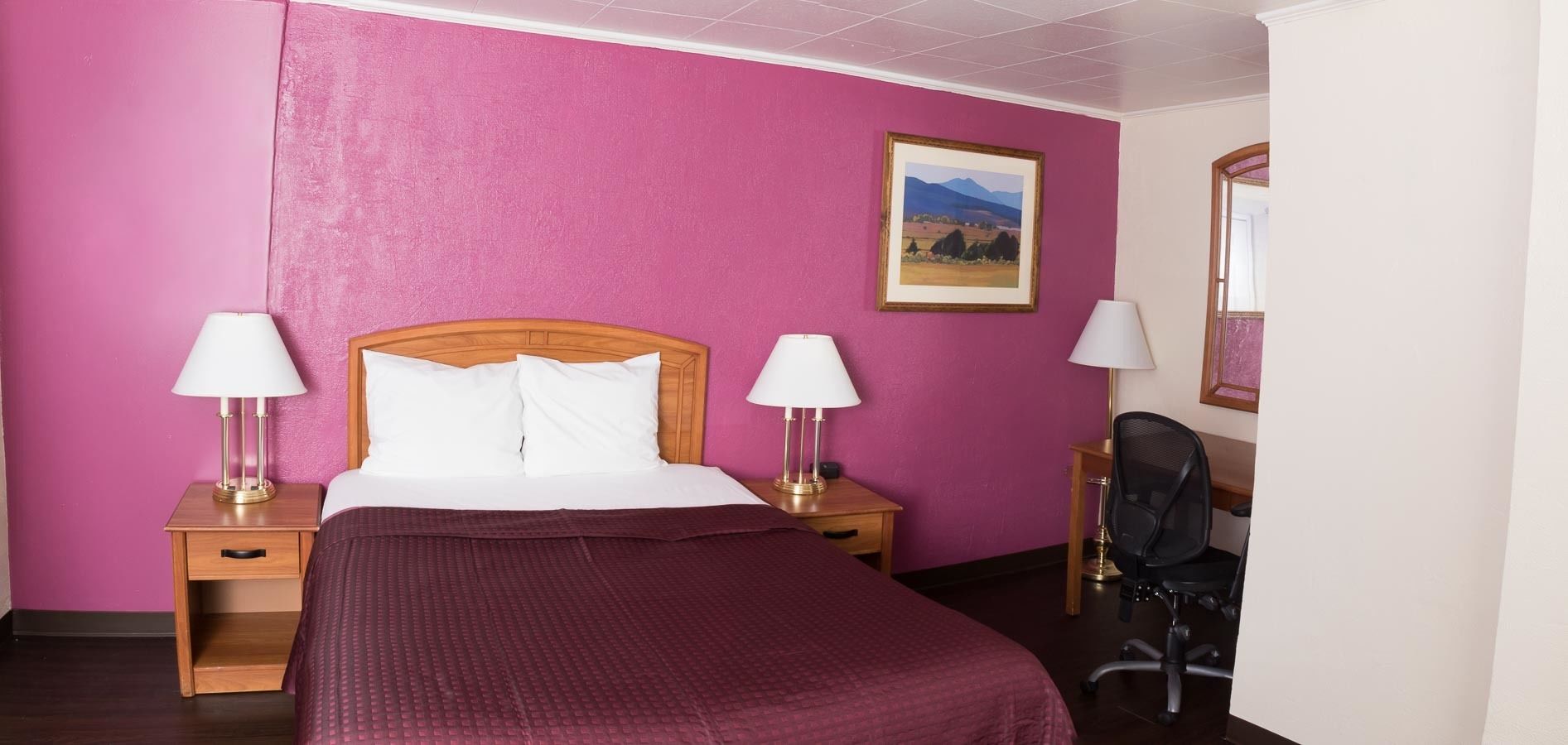 Een hotelkamer met een bed, twee nachtkastjes met lampen, een stoel en een schilderij aan de muur.