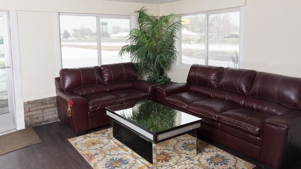 A living room with a dark brown leather sectional sofa, a glass coffee table, and a patterned rug. - Budget Inn (Caldwell)
