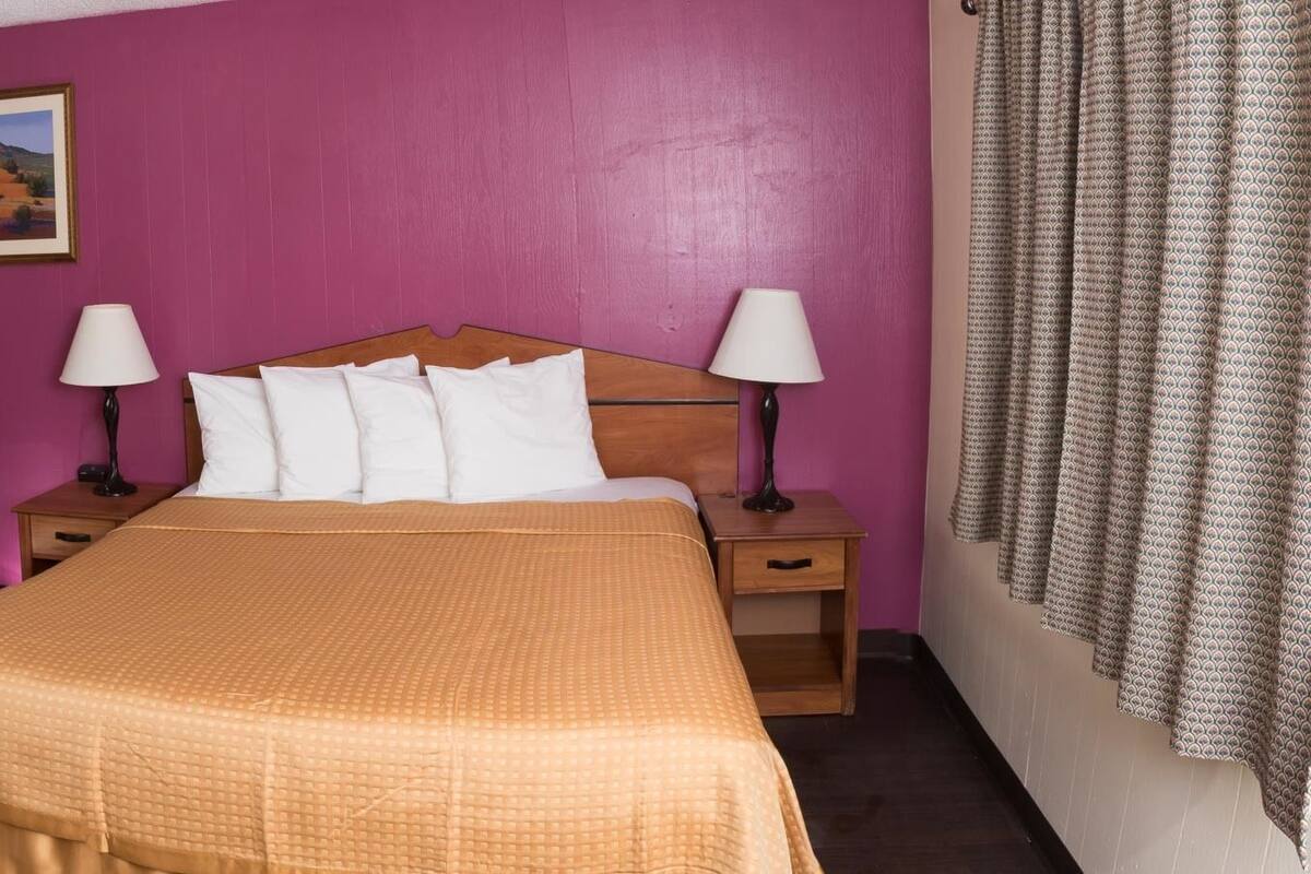 Une chambre d’hôtel comprenant un lit, deux tables de chevet avec des lampes, une chaise, un bureau, un miroir et un tableau au mur.