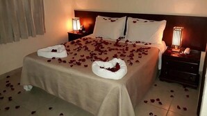 A hotel room with a bed covered in rose petals, two fish wall art, and bedside lamps.