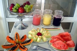 Une table avec un plateau de fruits, des fruits coupés en tranches et trois jus de fruits.