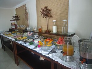 A buffet setup with various food items and beverages, including fruits, pastries, and a juice dispenser. - Hotel Casarão Pitangueiras (Guarujá)