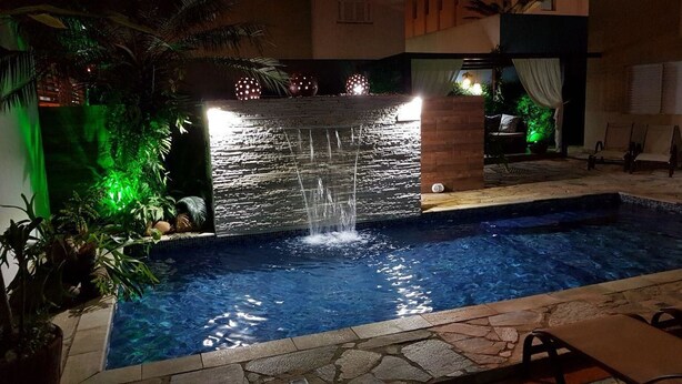 A swimming pool with a waterfall feature, surrounded by stone tiles and potted plants.