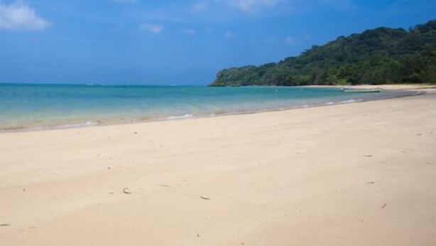 Une plage avec une eau d’un bleu limpide et un rivage sablonneux.