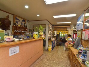 Un espace d’accueil avec un comptoir, des étagères remplies de divers articles et une porte donnant sur une autre pièce.