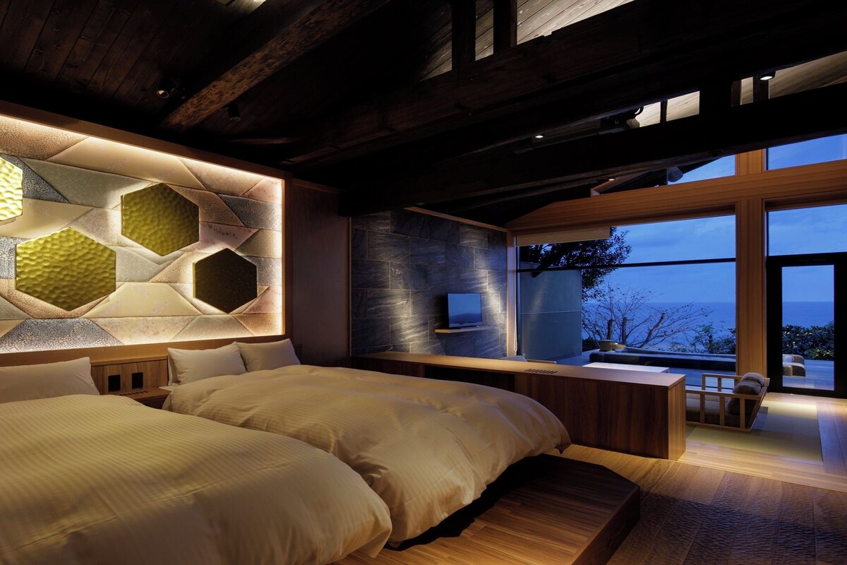 A modern bedroom with a large bed, a TV, and a view of the outdoors.
