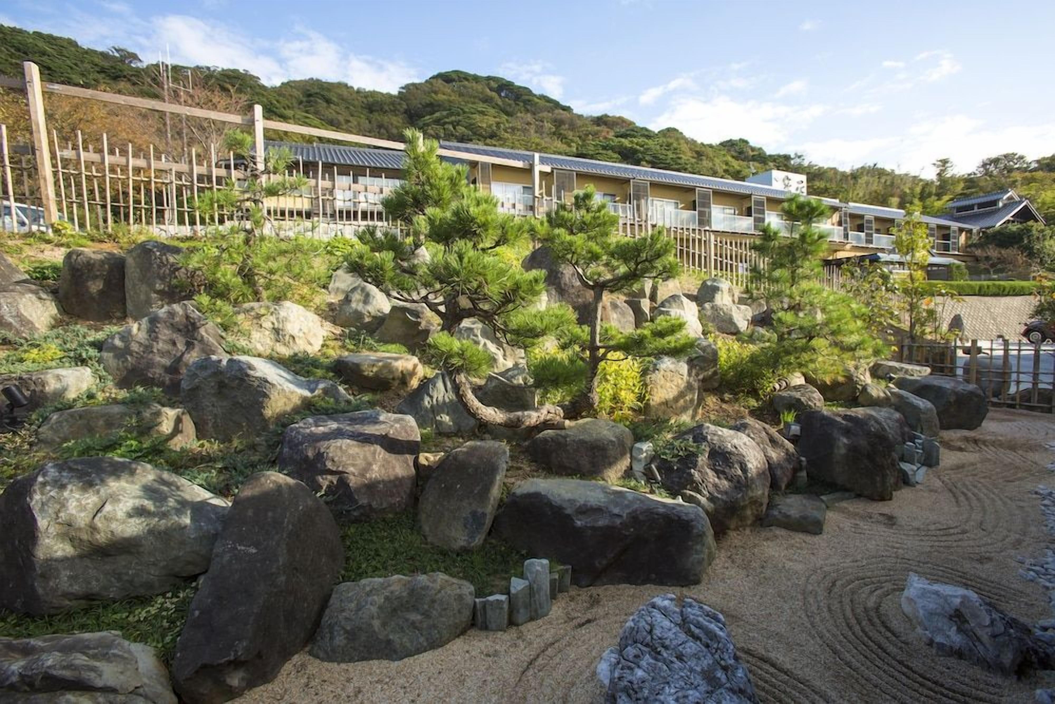 A traditional Japanese-style building with a garden featuring rocks and pine trees.
