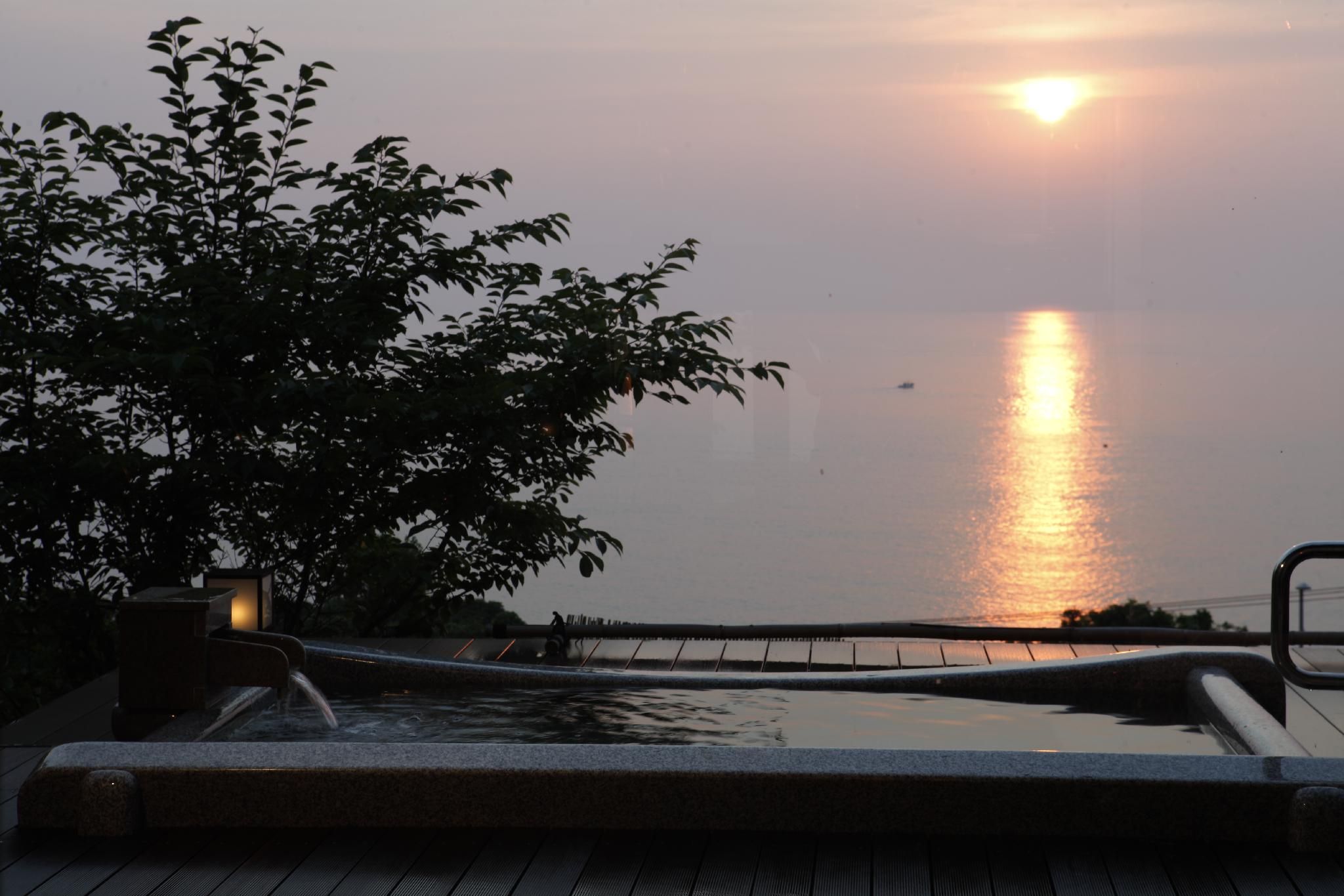A pool area with a view of the sunset over water, surrounded by foliage.