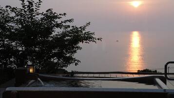 A pool area with a view of the sunset over water, surrounded by foliage.