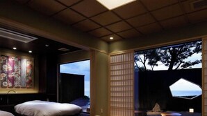 A modern hotel room with a large wooden table, comfortable seating, a view of the outdoors, and traditional decor. - Taiza Onsen Sumihei (Kyotango)