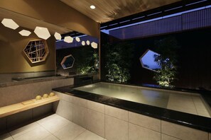 Een moderne badkamer met een groot bad, zeshoekige ramen en een houten plank met decoratieve objecten.