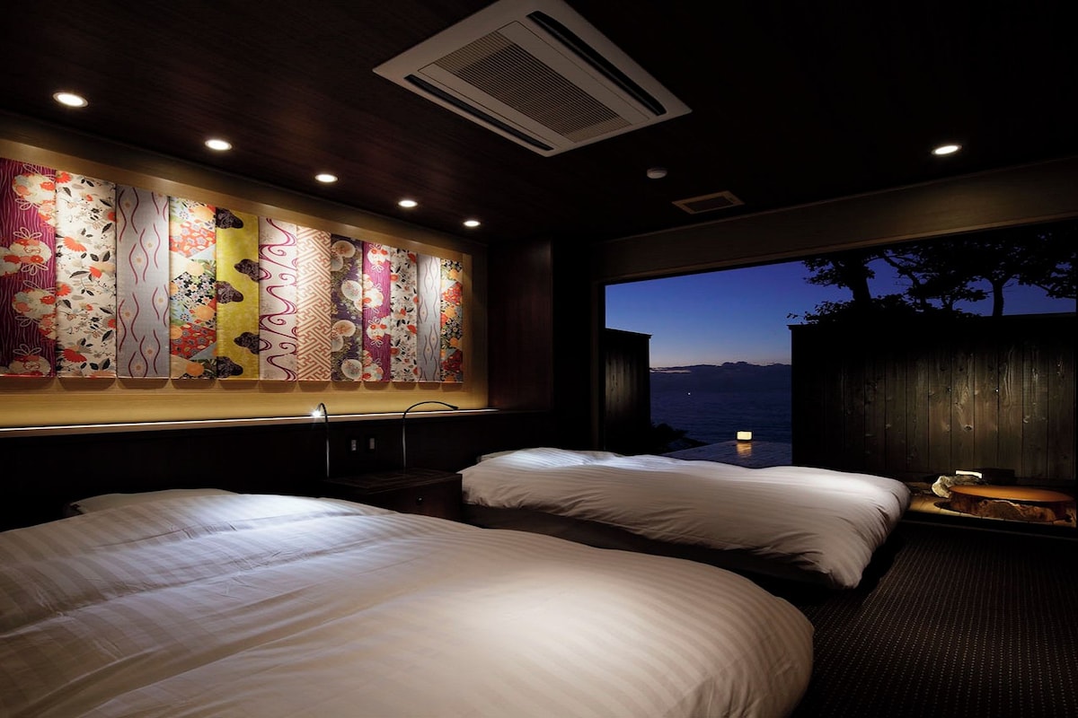 A hotel room with two beds, a large window with a view of the sea, and a wall with a decorative panel.