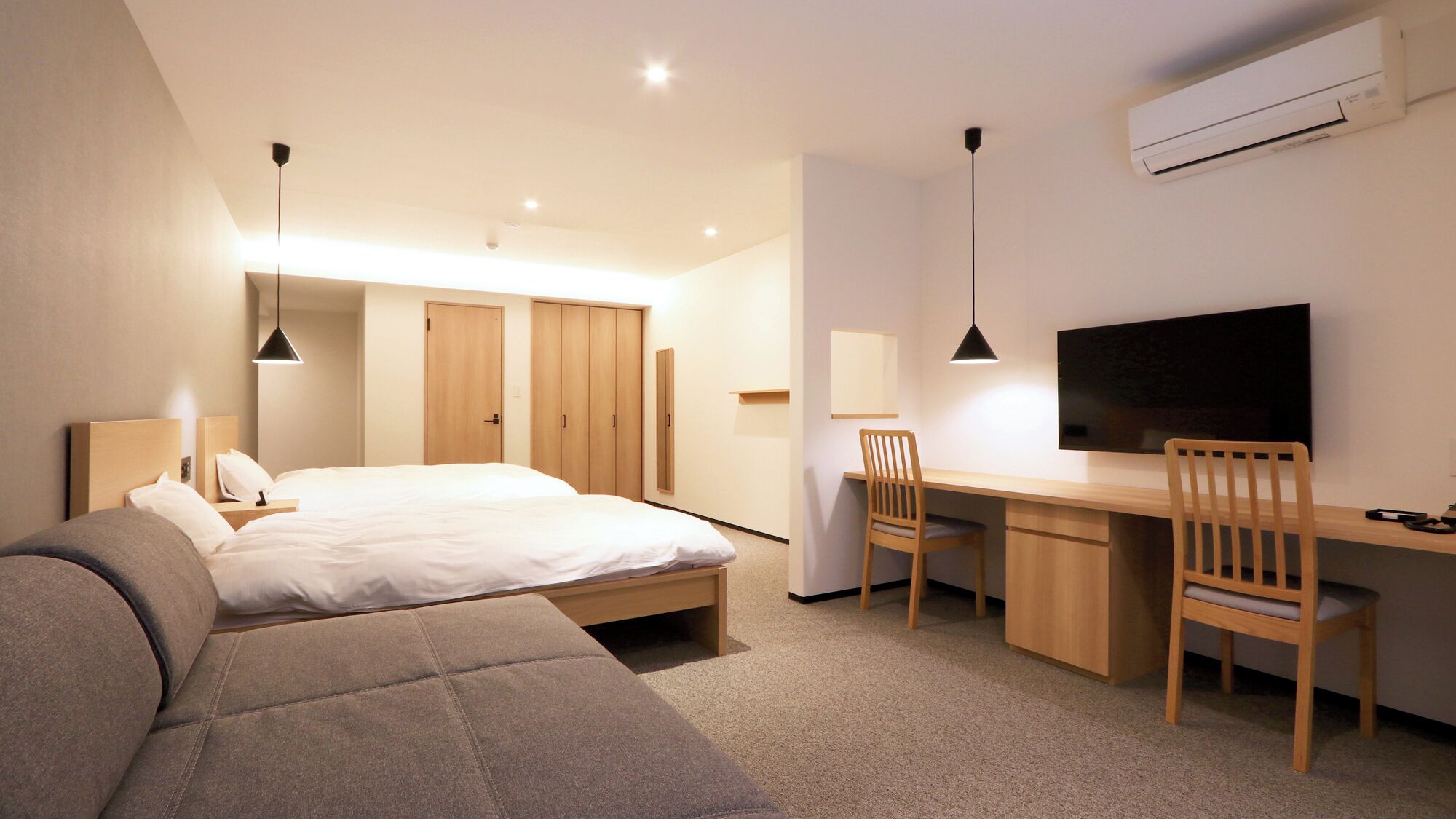 A modern hotel room with a bed, a desk, a chair, a TV, and a wardrobe.