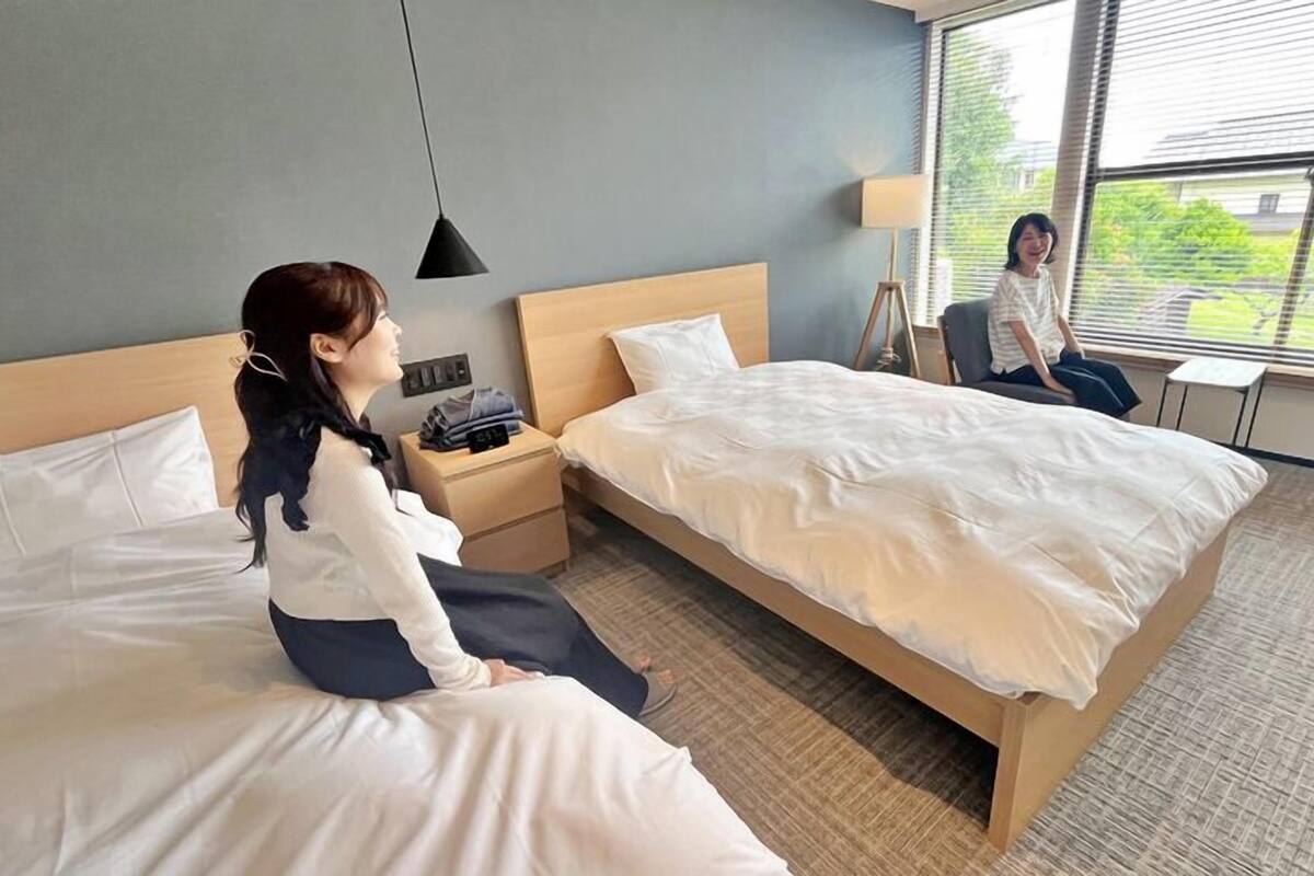 Une chambre d’hôtel avec deux lits, une table de chevet, une lampe et une fenêtre donnant sur un paysage verdoyant.