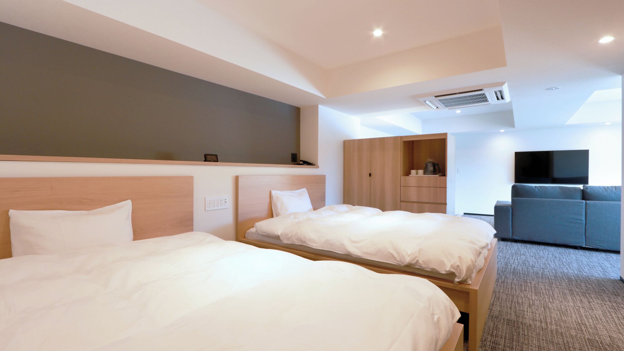 A hotel room with two beds, a TV, a sofa, and a wardrobe.