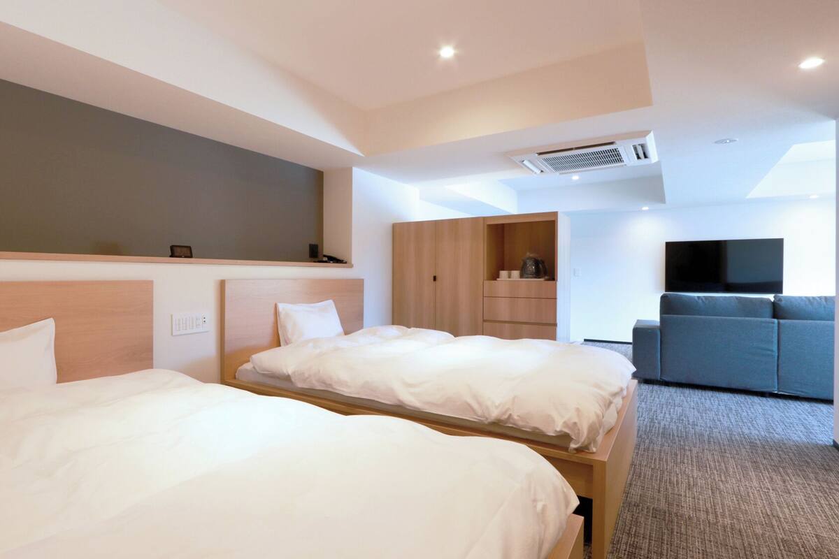 Une chambre d’hôtel avec deux lits, une télévision, un canapé et une armoire.