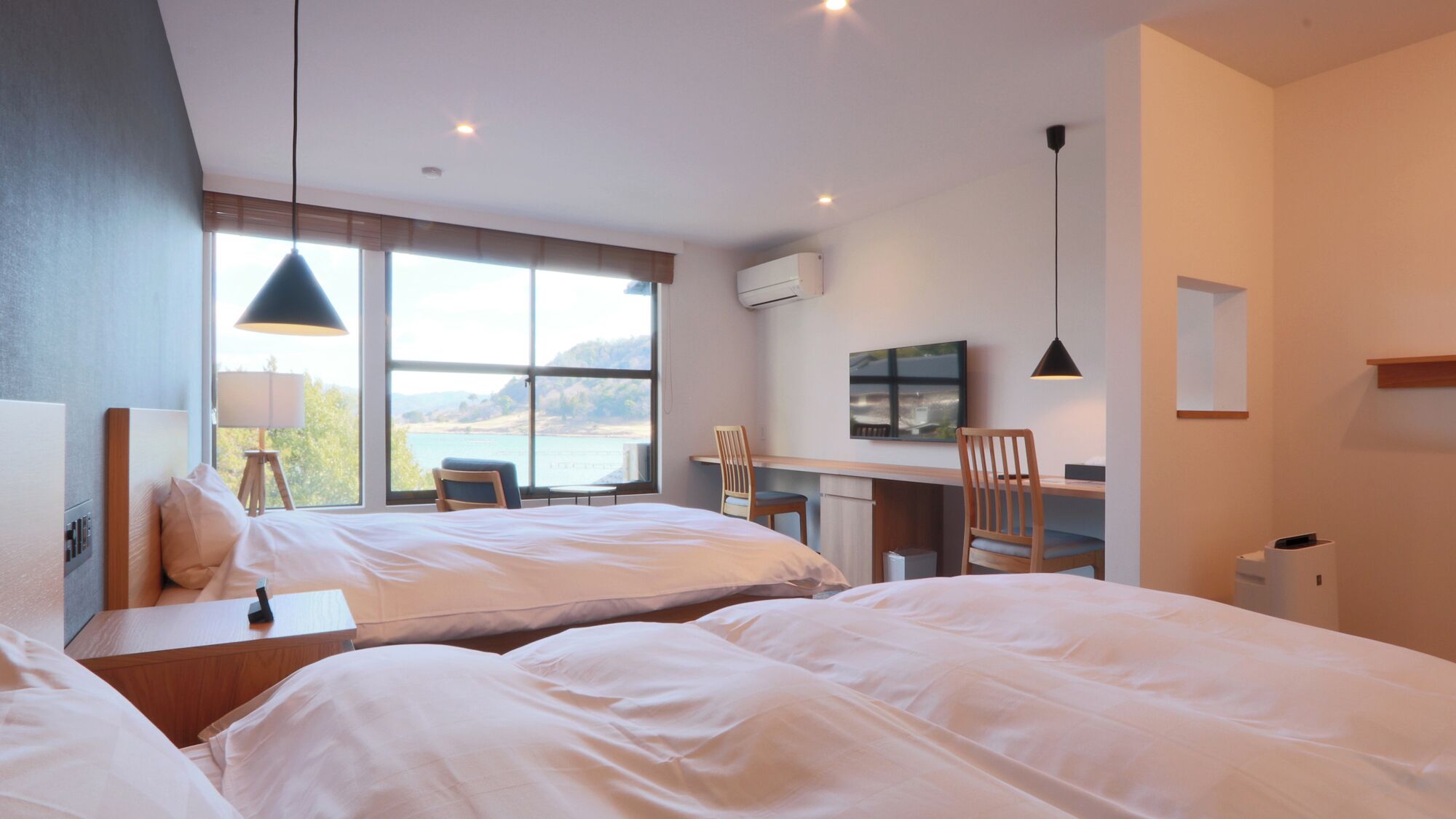 A hotel room with two beds, a desk, a chair, a TV, and a window with a view.