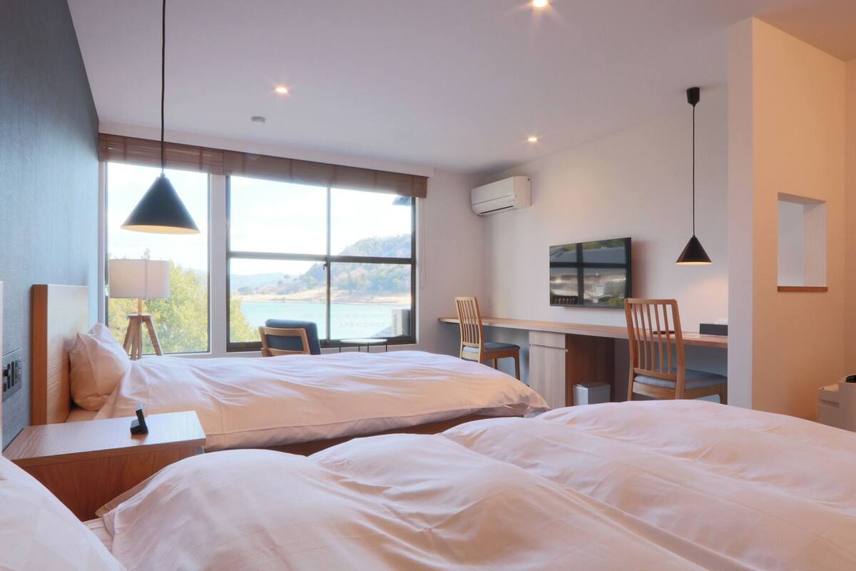 Une chambre d’hôtel avec deux lits, un bureau, une chaise, une télévision et une fenêtre donnant sur un beau paysage.