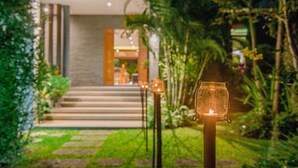 A pathway leading to a building with a glass door, surrounded by greenery and a candle on a stand. - Moin Lakeside Pool Villa ChiangMai (Hang Dong)