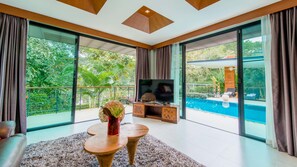 Uma sala de estar moderna com uma televisão grande, uma mesa de centro de madeira e vista para uma piscina.