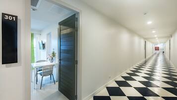 Un pasillo de hotel con suelo a cuadros blanco y negro, una puerta con la inscripción '301', y un área de comedor con una mesa y sillas.