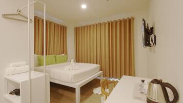 Una habitación de hotel con cama, una mesa con tetera, una silla y un perchero.