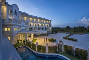 Un hotel moderno con piscina, varios balcones y una entrada bien iluminada.