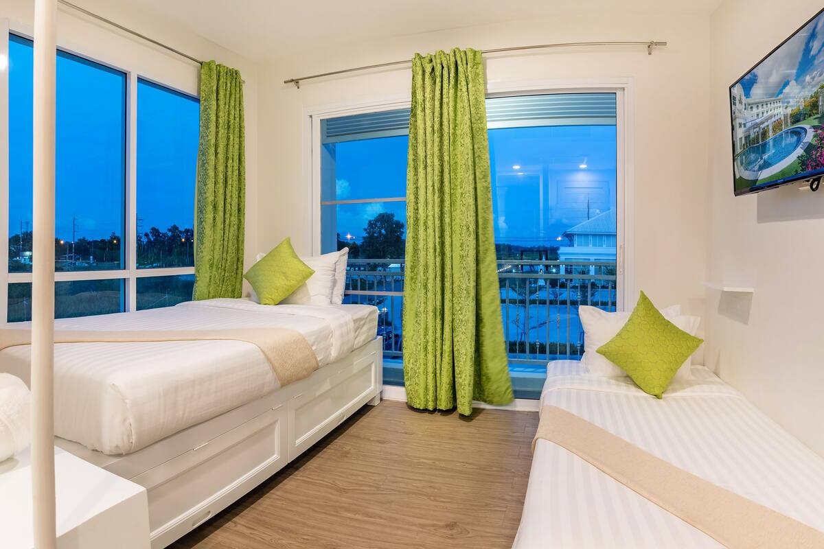 Quarto de hotel com duas camas, varanda, janelas amplas e um quadro na parede.